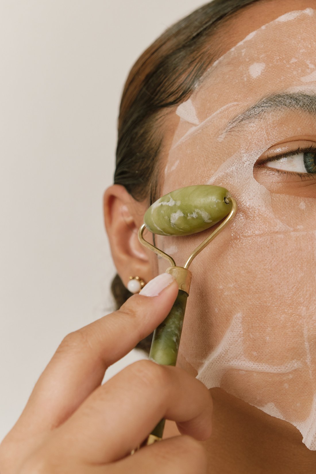 Woman Using a Jade Roller on Face with Sheet Mask